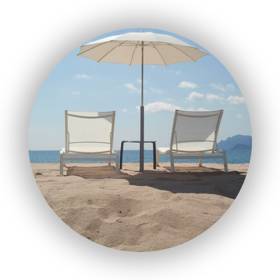 Two lounging chairs on a beach beneath a parasol.